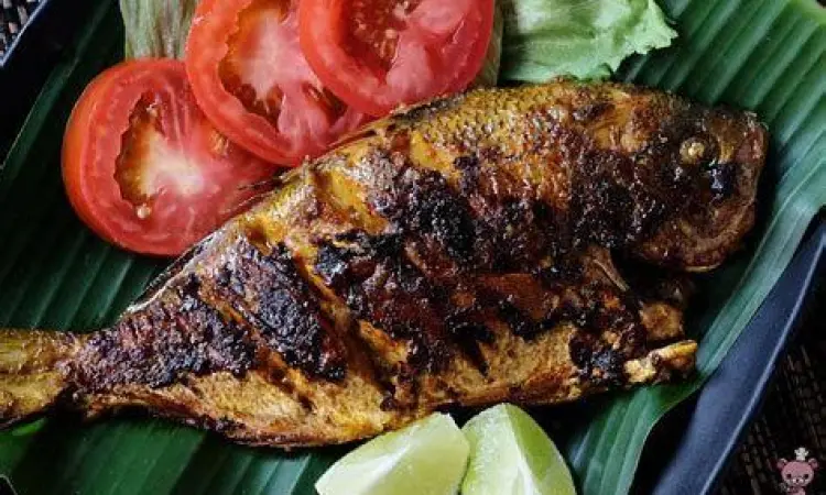 Proses pengolesan bumbu pada ikan yang sedang dibakar