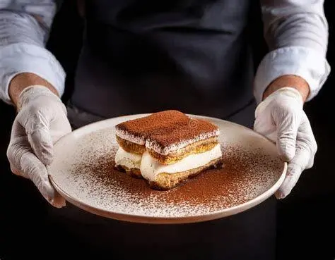 Penyajian Tiramisu Elegan Sajian satu porsi tiramisu di piring dengan taburan kakao