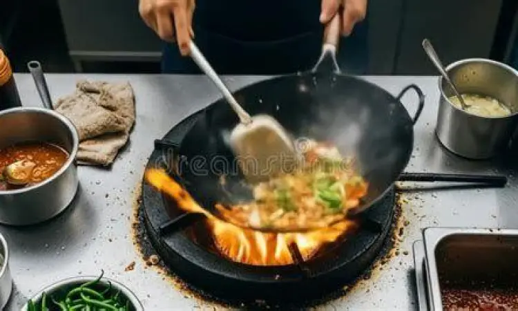Koki profesional melakukan teknik stir frying dengan api besar